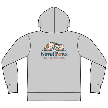 A light gray pullover hoodie shown from the back, featuring a 'Novel Paws' graphic printed on the center back. The graphic depicts a cartoon illustration of a sleeping dog and cat on an open book, with the text 'Novel Paws' in navy blue and smaller orange text below reading 'BOOKS • PETS • PEOPLE • RESCUE'.